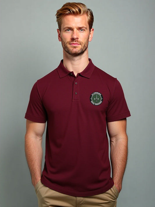 Male model wearing maroon 24 Commando polo shirt with embroidered military-style green and white badge, short sleeves, button-up collar, paired with beige trousers, casual uniform clothing product photo.