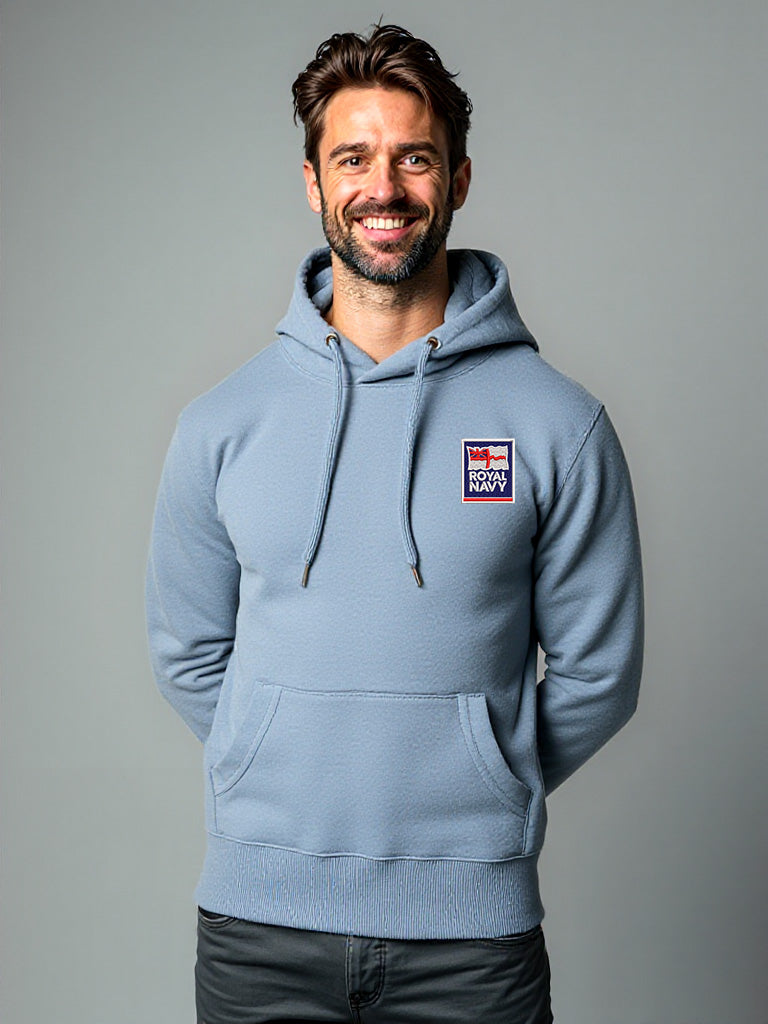 Male model wearing a stone blue hoodie with the Royal Navy logo embroidered on the left chest, hands in pockets, posed naturally.
