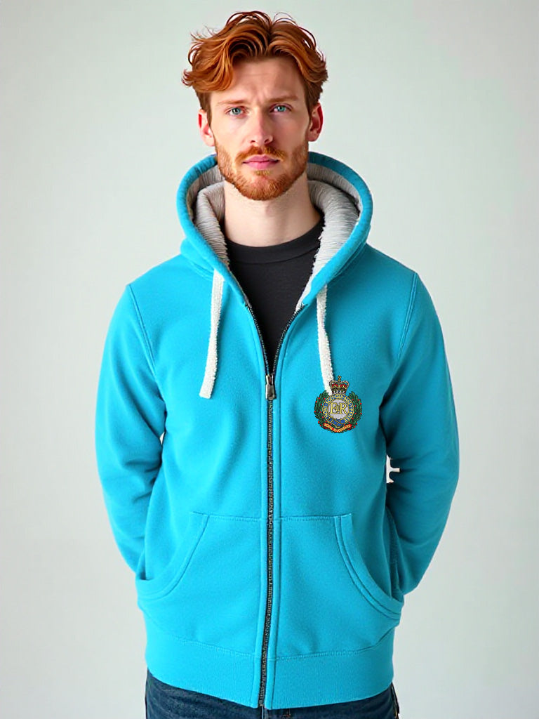 Man wearing a tropical blue zip-up hoodie with Royal Engineers crest on the chest, hands in pockets, standing against a pale background.